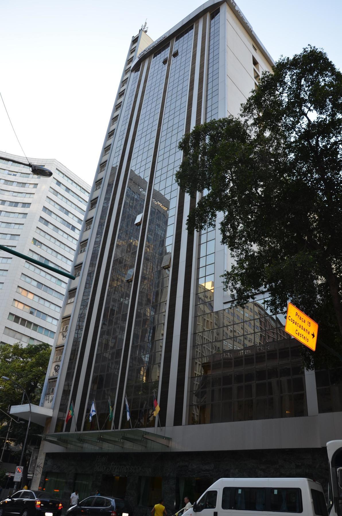 Hotel Atlantico Tower Rio de Janeiro Exterior foto The photo shows a city street with tall buildings. In the foreground, there is a modern glass skyscraper featuring reflective surfaces and vertical lines. Next to it, there's another building with a different architectural style, also made of glass. 